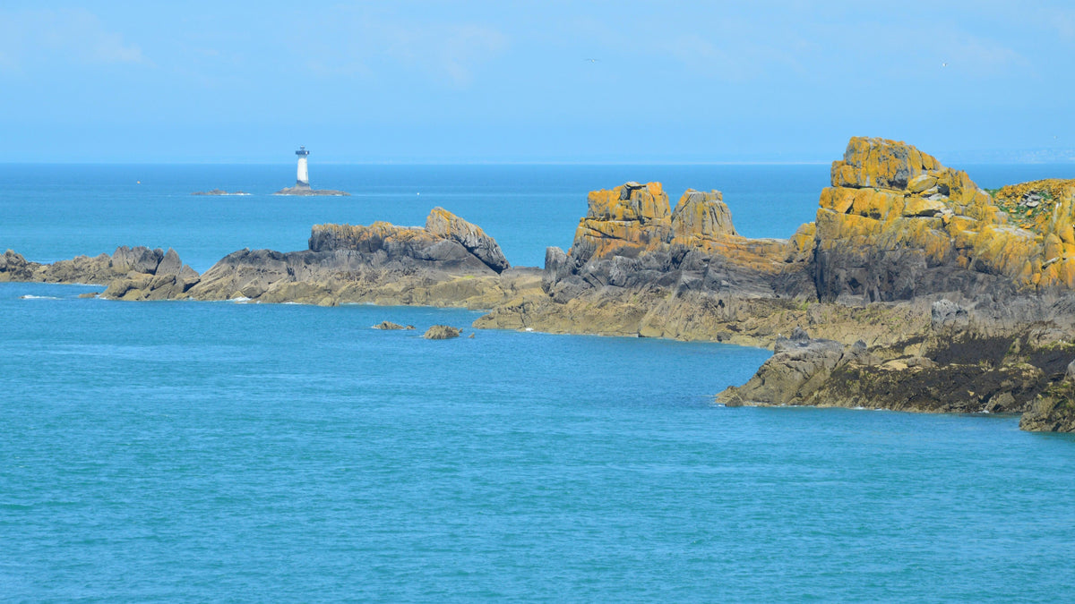Côte rocheuse bretonne avec un phare au large et une mer turquoise